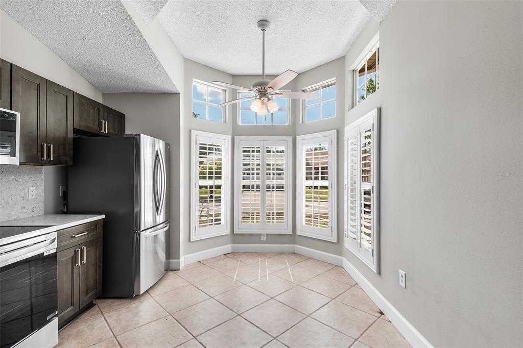 A kitchen breakfast nook features tile flooring, dark cabinetry, a ceiling fan, and bay windows — 4011 LEVONSHIRE PLACE, VALRICO, FL