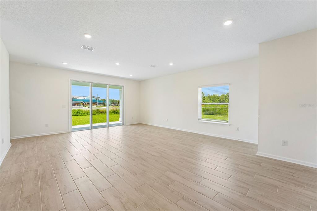 An empty living room features light wood-look tile flooring, white walls, and sliding glass doors — 373 SILVER LILY WAY, ST AUGUSTINE, FL