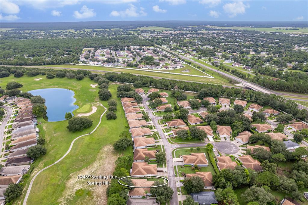 An aerial view shows a residential neighborhood with houses, a golf course, and a lake — 14459 STERLING RUN, SPRING HILL, FL