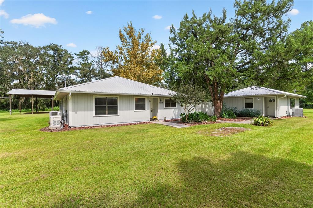 A wide shot of a light-colored house with a metal roof on a grassy lot — 16310 NW 40TH PLACE, NEWBERRY, FL