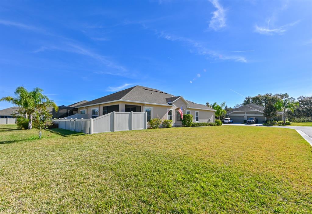 A tan single-story house with a fenced backyard and a large lawn under blue skies — 13529 CREST LAKE DR, HUDSON, FL