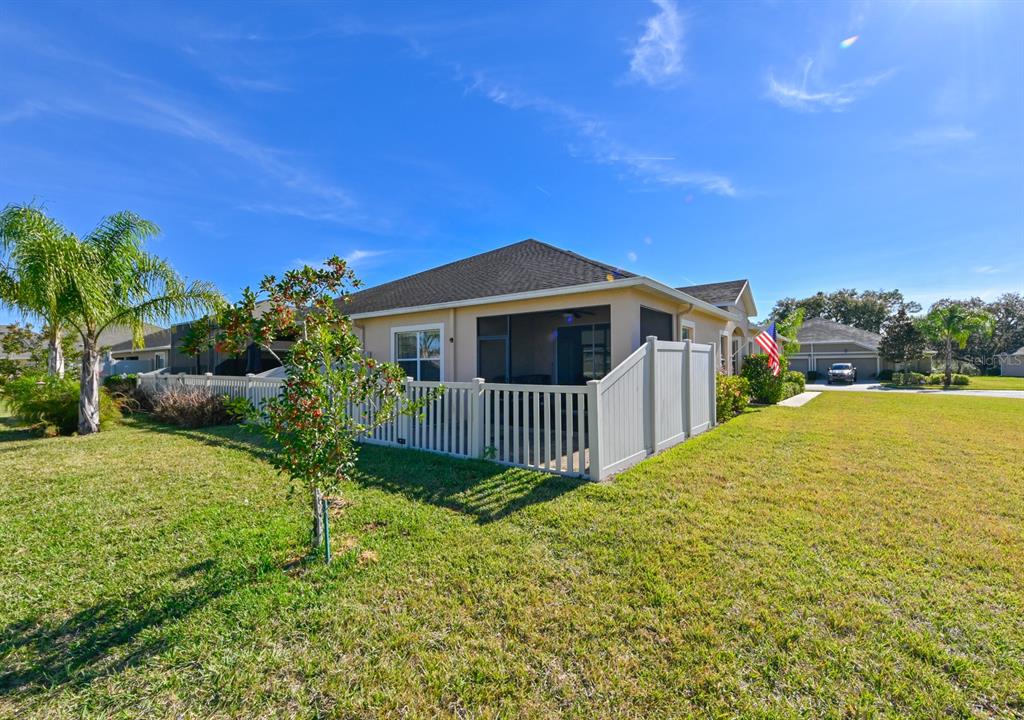 A tan house with a screened-in porch and white vinyl fencing sits on a lawn — 13529 CREST LAKE DR, HUDSON, FL