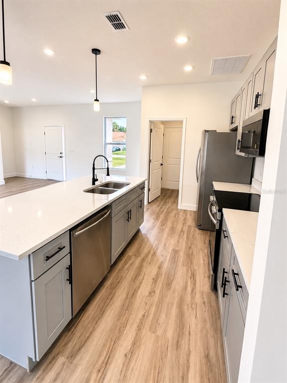 A modern kitchen features light gray cabinets, white countertops, stainless steel appliances, and wood-look flooring — 441 CARAWAY DRIVE, KISSIMMEE, FL