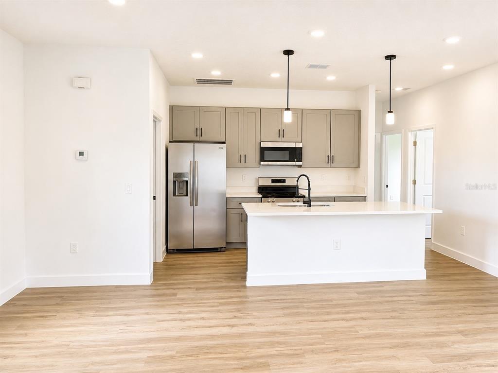 A modern kitchen features gray cabinets, stainless steel appliances, a white island, and wood-look flooring — 441 CARAWAY DRIVE, KISSIMMEE, FL