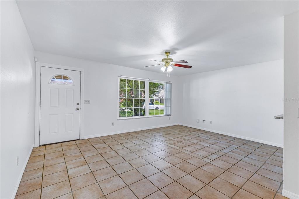 An empty room features white walls, a tiled floor, a ceiling fan, and a front door — 9148 DUBOIS BOULEVARD, ORLANDO, FL