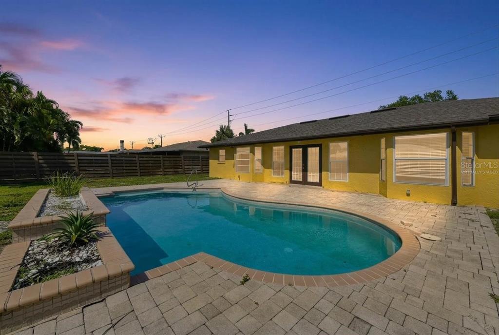 A backyard features a swimming pool with a raised planter and a yellow house exterior — 1304 71ST STREET NW, BRADENTON, FL