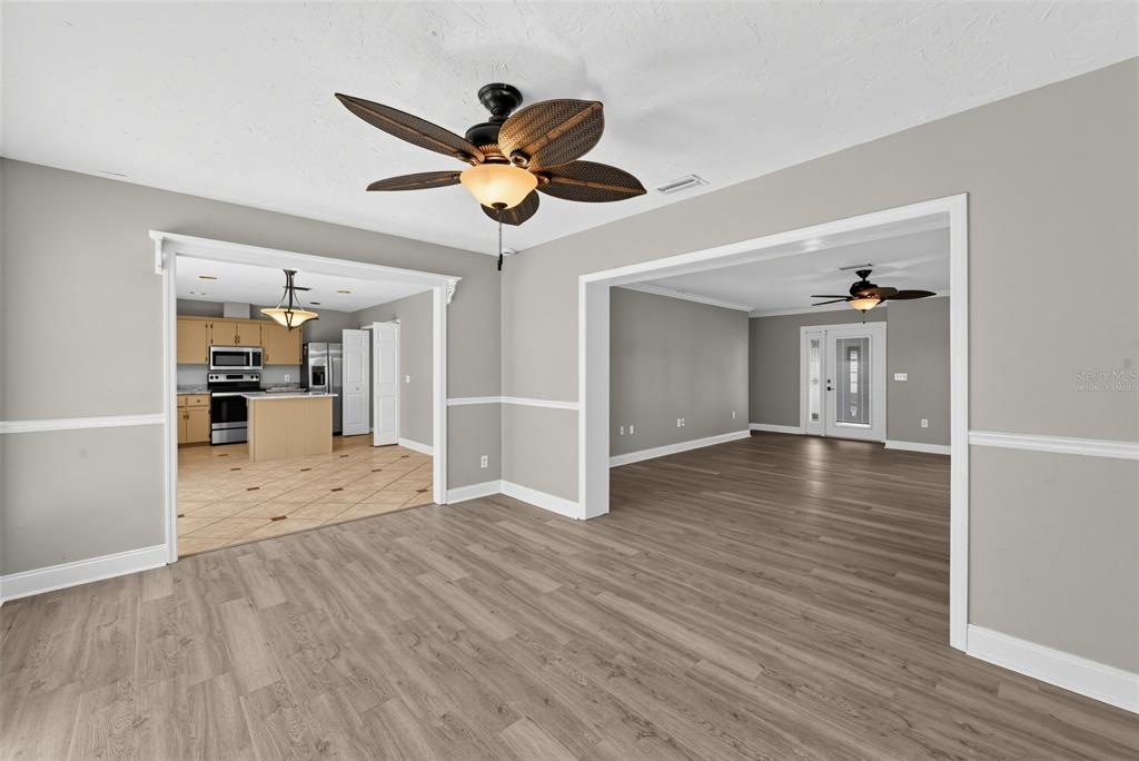 A living area with wood-look flooring, a ceiling fan, and views into a kitchen and room — 1304 71ST STREET NW, BRADENTON, FL