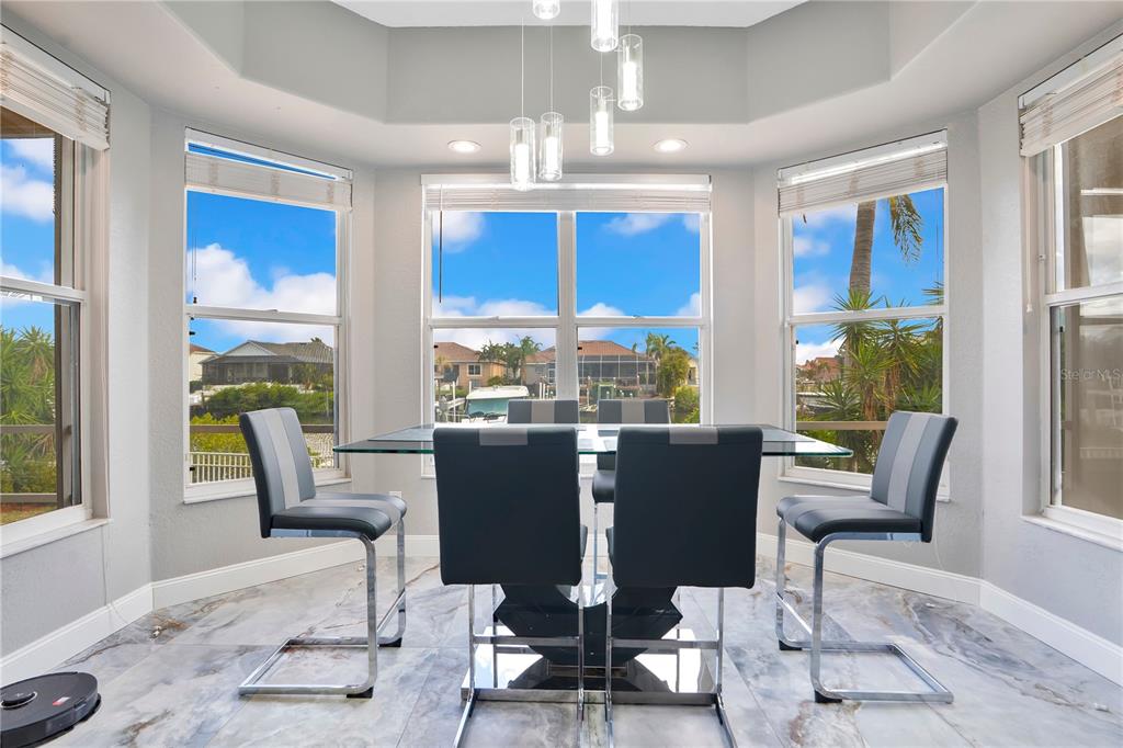 A dining area features a glass table, modern chairs, marble floors, and large bay windows — 934 SYMPHONY ISLES BOULEVARD, APOLLO BEACH, FL