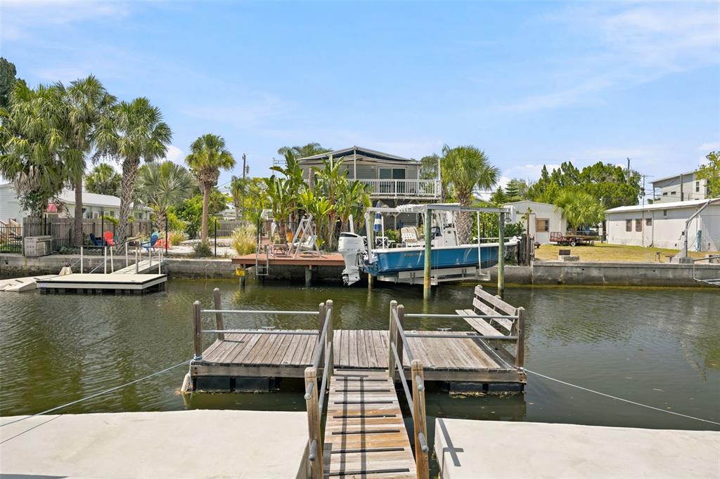 A wooden floating dock sits in a canal in front of a house with a boat — 7037 MCCRAY DRIVE, HUDSON, FL