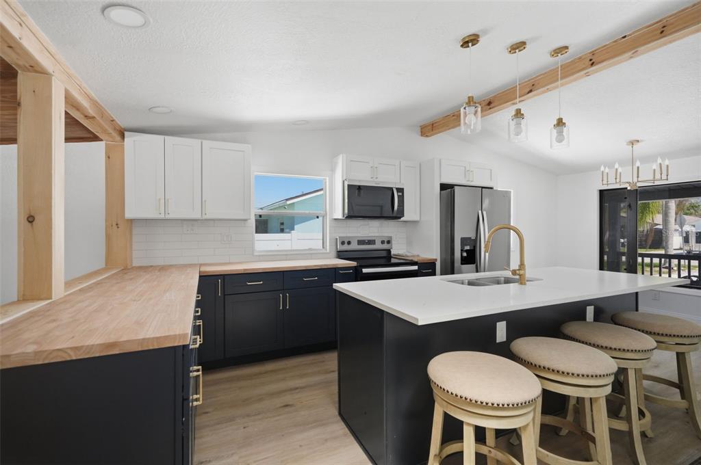 A kitchen features dark lower cabinets, white upper cabinets, wood countertops, and a central island — 7037 MCCRAY DRIVE, HUDSON, FL