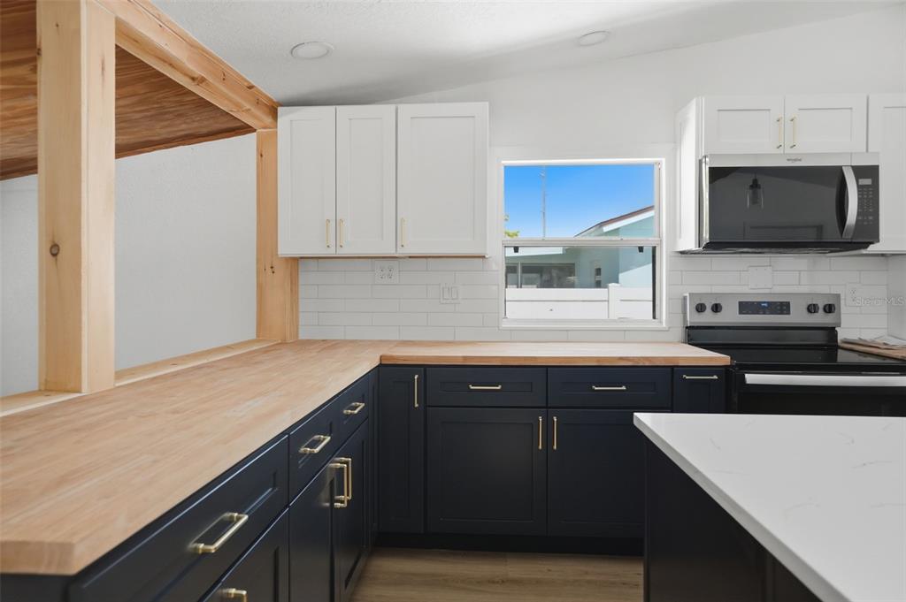 A kitchen features dark blue lower cabinets, white upper cabinets, and light wood countertops — 7037 MCCRAY DRIVE, HUDSON, FL