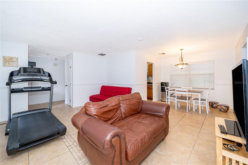 A living room features tile flooring, a brown leather sofa, a red futon, and a treadmill — 103 KILKENNY COURT, LONGWOOD, FL