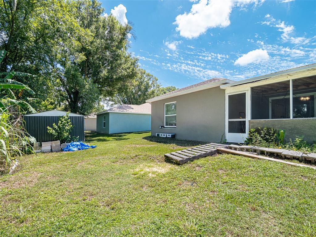 A backyard view showing a house with a screened porch, a metal shed, and grass — 151 1ST STREET, WINTER HAVEN, FL