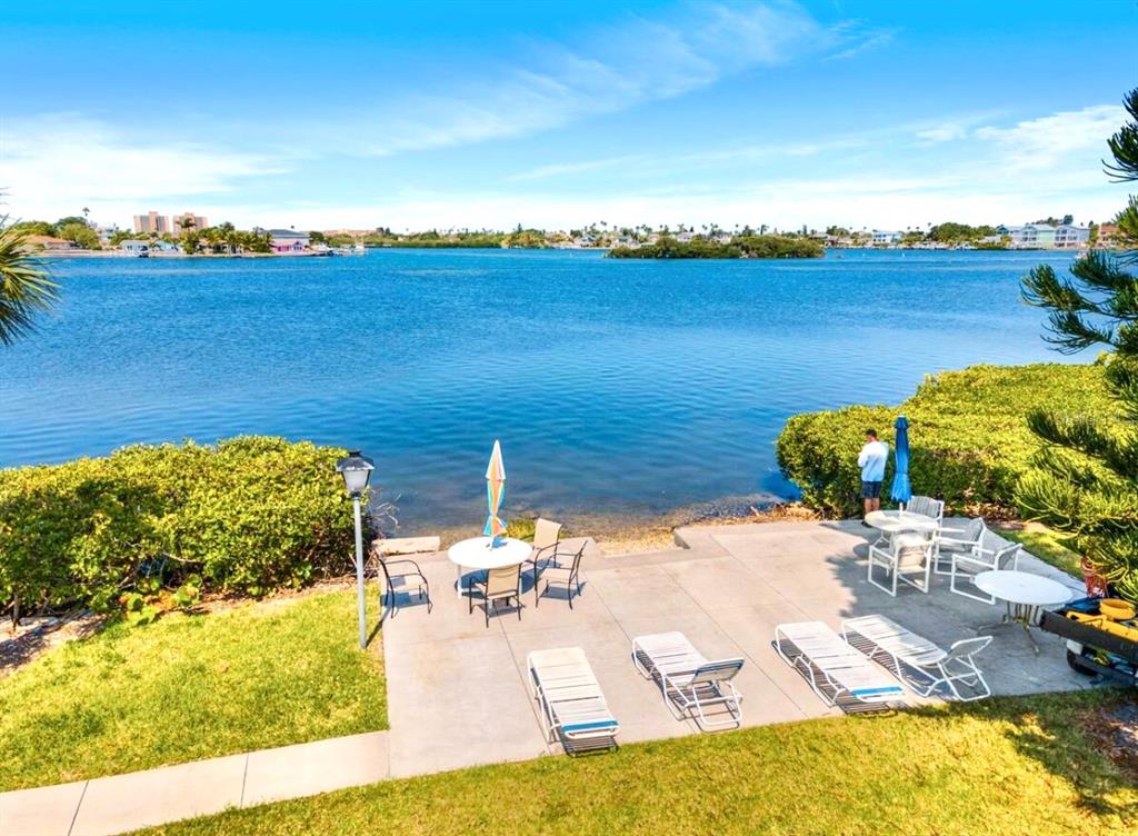 A concrete patio with lounge chairs and tables overlooks a calm bay with distant buildings — 12760 INDIAN ROCKS ROAD UNIT 903, LARGO, FL