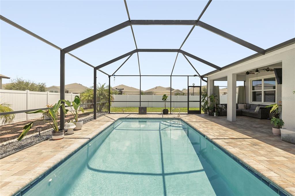 A rectangular swimming pool sits inside a screened-in patio with paver decking and a fence — 13301 WATERLEAF GARDEN CIRCLE, RIVERVIEW, FL