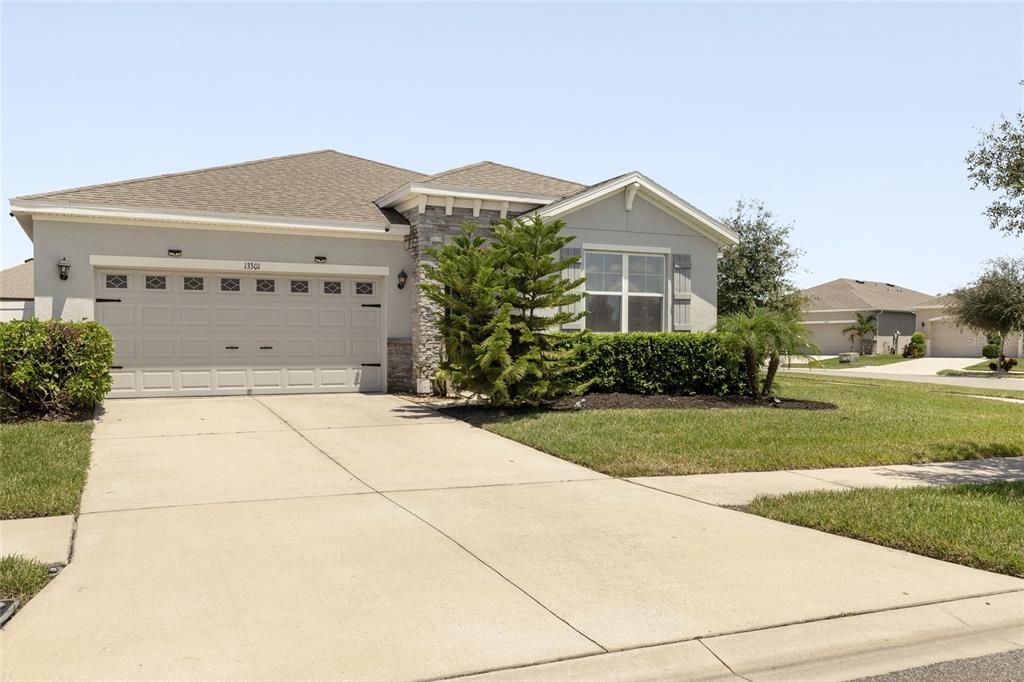 A single-story suburban house with a beige stucco exterior, stone accents, and a two-car garage — 13301 WATERLEAF GARDEN CIRCLE, RIVERVIEW, FL
