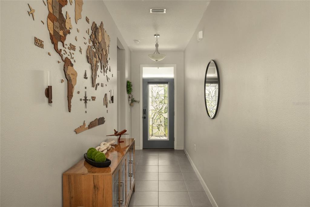 A hallway features a wooden world map wall art, a console table, and a glass-paneled door — 13301 WATERLEAF GARDEN CIRCLE, RIVERVIEW, FL