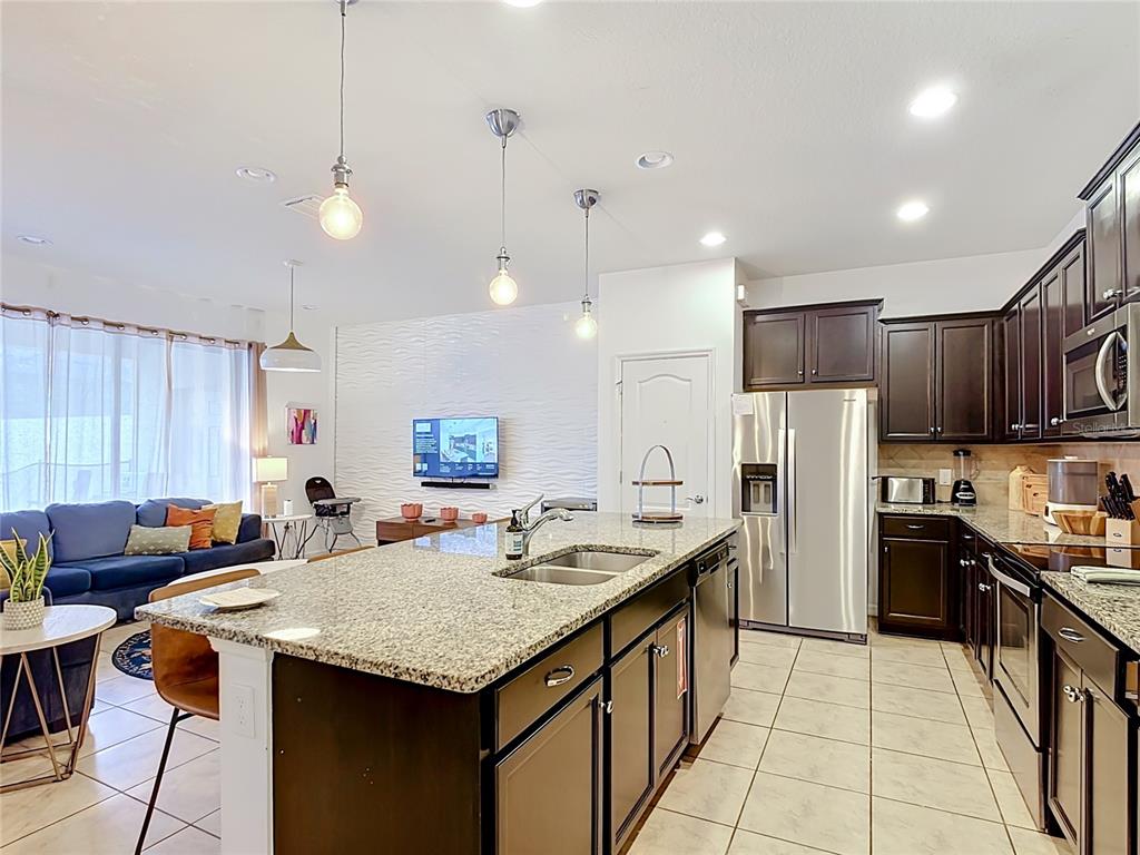 A kitchen with a granite island and dark cabinets opens into a living room area — 8891 GENEVE COURT, KISSIMMEE, FL