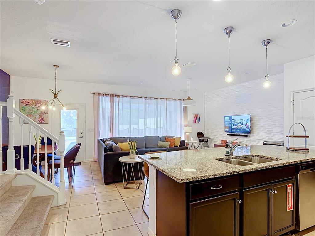 An open-concept kitchen with a granite island overlooks a living area with a textured wall — 8891 GENEVE COURT, KISSIMMEE, FL