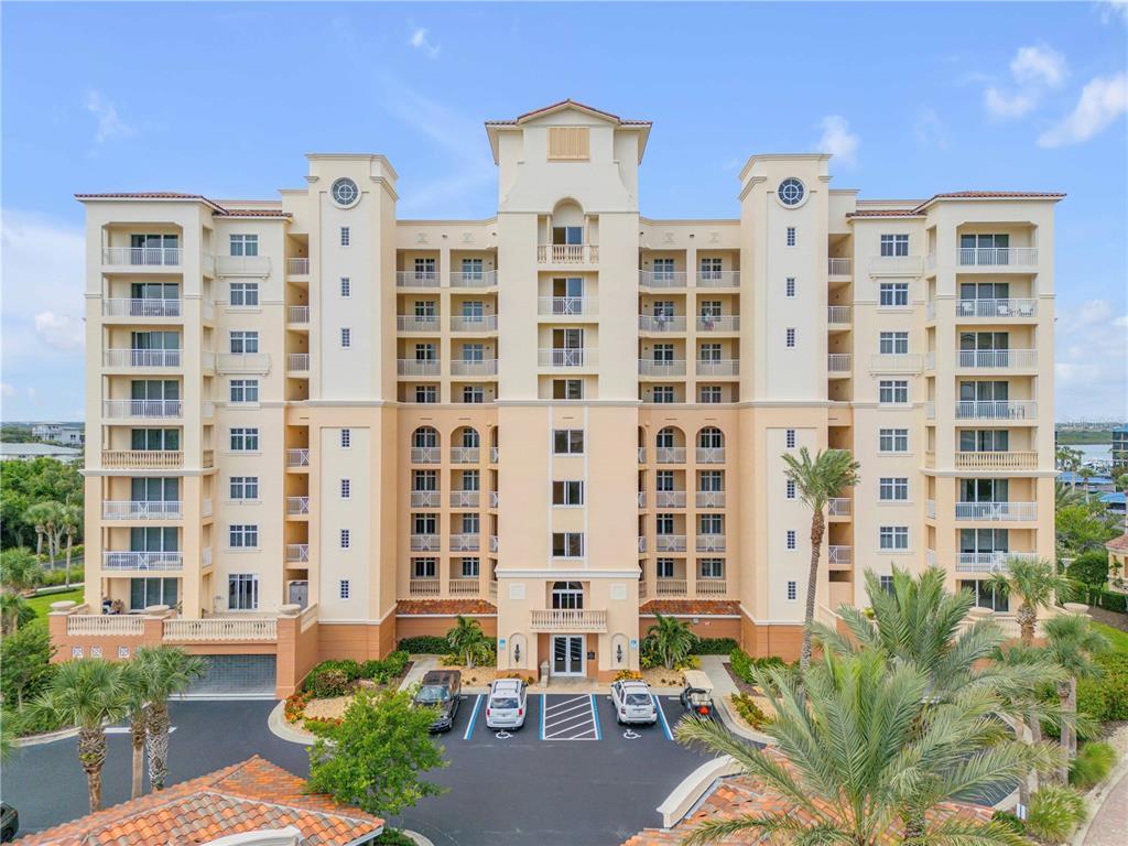 A multi-story beige apartment building with balconies and a parking lot in front — 265 MINORCA BEACH WAY UNIT 404, NEW SMYRNA BEACH, FL