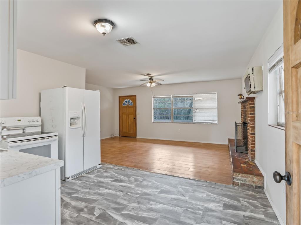 A kitchen with gray vinyl flooring opens into a living area with wood floors and fireplace — 8935 CR 647S, BUSHNELL, FL