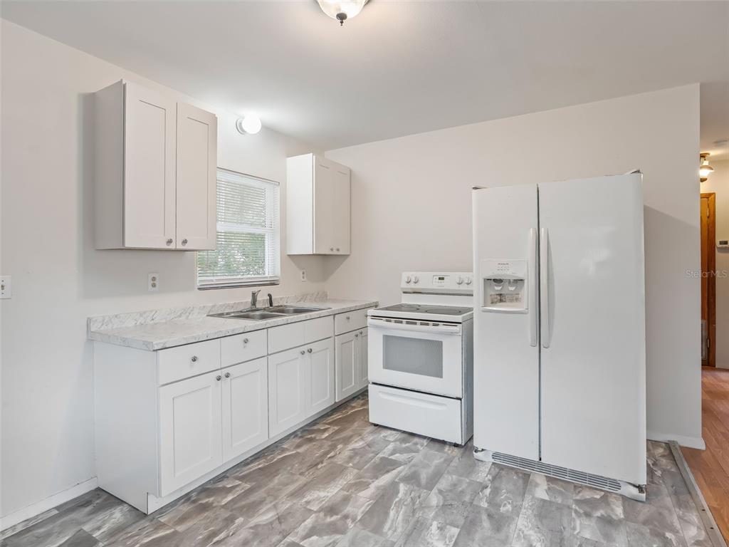 A kitchen with white cabinets, white appliances, marble-look countertops, and gray wood-look flooring — 8935 CR 647S, BUSHNELL, FL