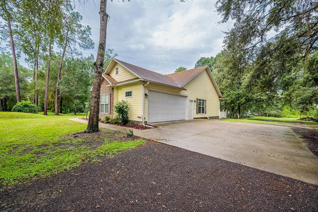 A yellow house with a two-car garage and a concrete driveway surrounded by trees — 486 LAKESHORE DRIVE, STARKE, FL
