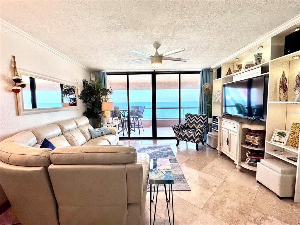 A living room features a beige sofa, patterned armchair, and large windows overlooking the ocean — 1310 GULF BOULEVARD UNIT 18B, CLEARWATER, FL