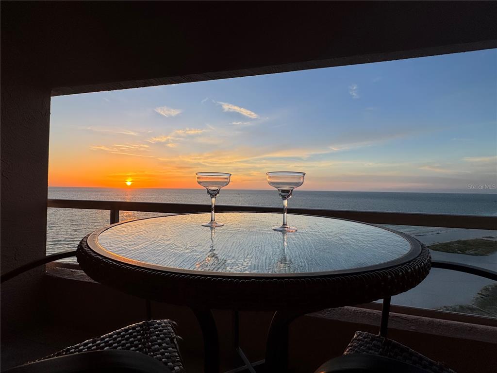 A balcony table with two glasses overlooks the ocean during a sunset — 1310 GULF BOULEVARD UNIT 18B, CLEARWATER, FL