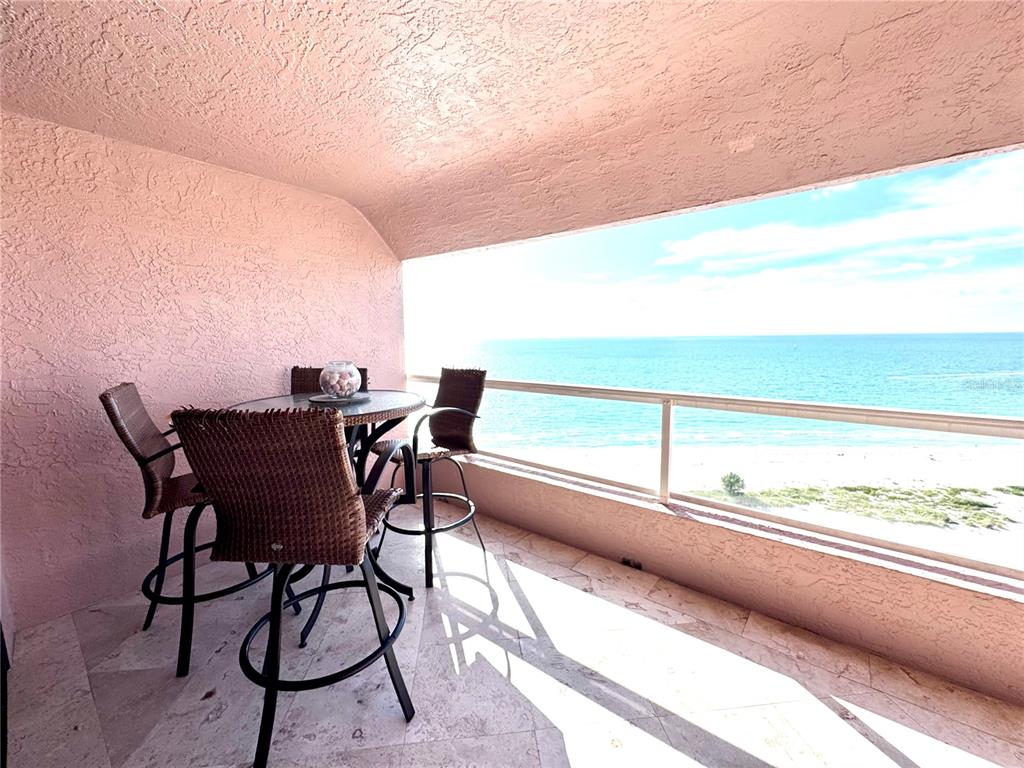 A balcony with a table and chairs overlooks the ocean with a pink textured wall — 1310 GULF BOULEVARD UNIT 18B, CLEARWATER, FL