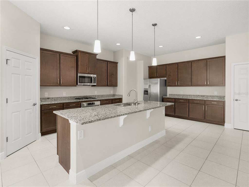 A kitchen features dark wood cabinets, granite countertops, a central island, and light tile flooring — 4212 RUTHANN CIRCLE, MELBOURNE, FL