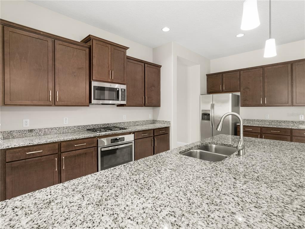 A kitchen features dark wood cabinets, granite countertops, stainless steel appliances, and a central island — 4212 RUTHANN CIRCLE, MELBOURNE, FL