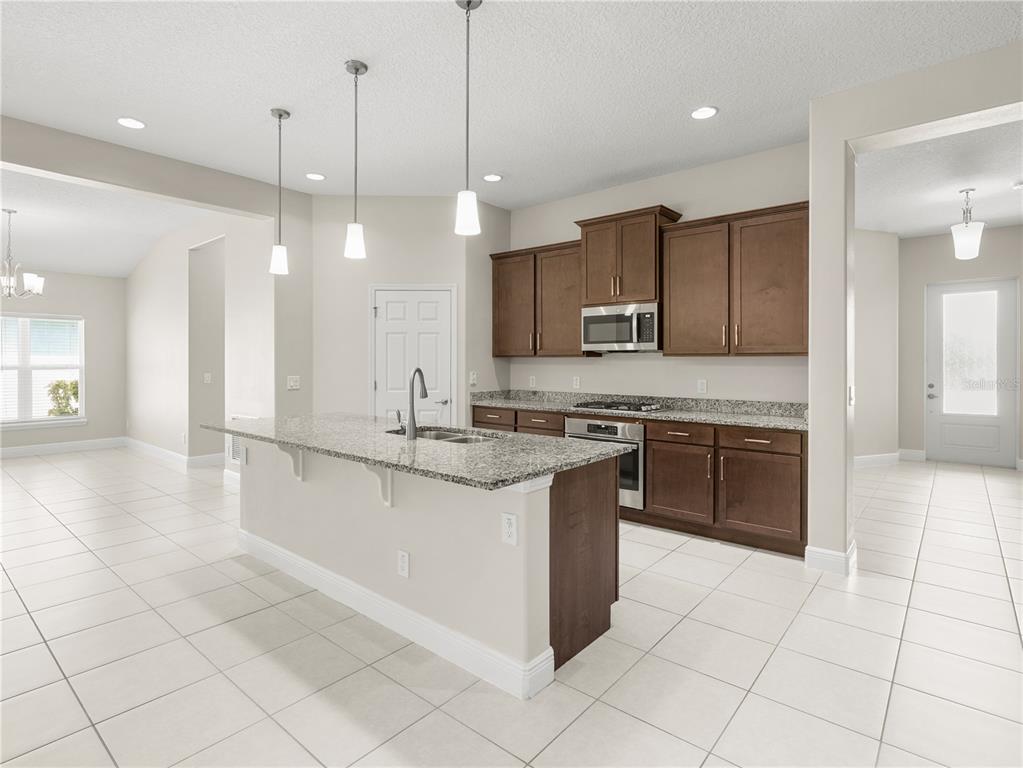 A kitchen features dark wood cabinets, granite countertops, a center island, and light tile flooring — 4212 RUTHANN CIRCLE, MELBOURNE, FL