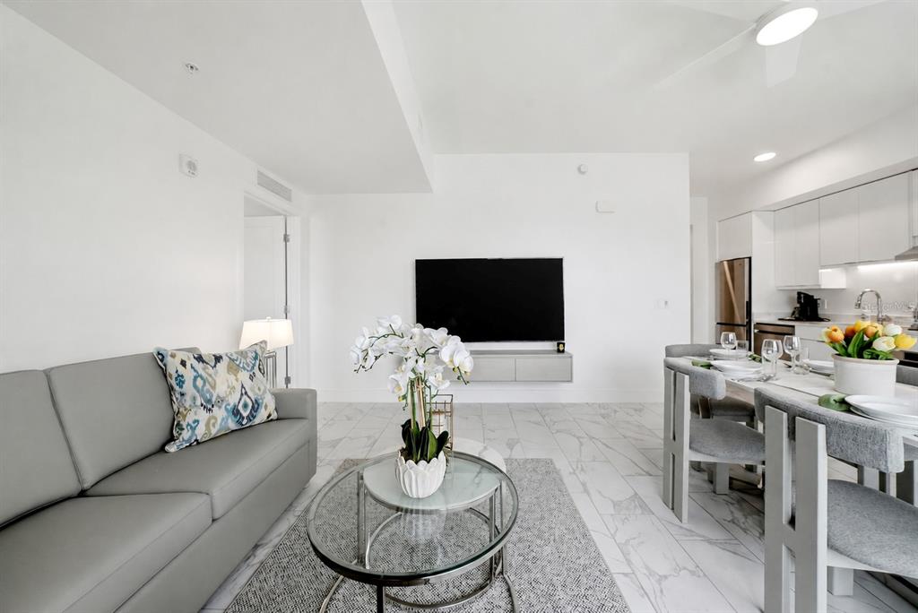 A modern living and dining area with white walls, marble-look tile floors, and gray furniture — 411 E SHORE DRIVE UNIT 206, CLEARWATER BEACH, FL
