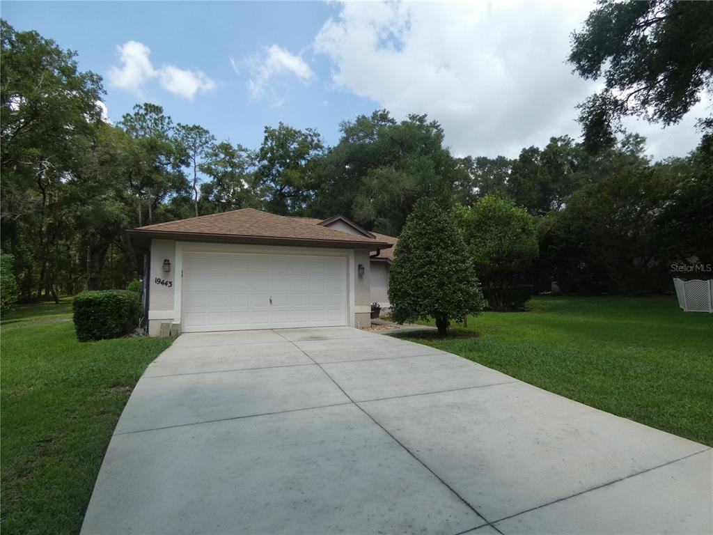 A single-story house with a white garage door and a concrete driveway surrounded by trees — 19443 SW 101ST PLACE ROAD, DUNNELLON, FL