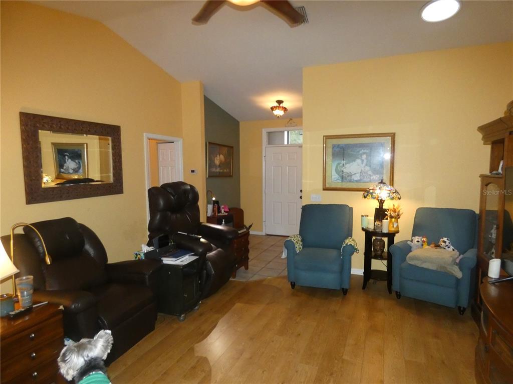 A living room features yellow walls, wood flooring, a vaulted ceiling, and several armchairs — 19443 SW 101ST PLACE ROAD, DUNNELLON, FL