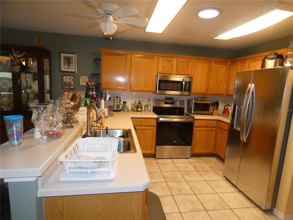 A kitchen features light wood cabinets, stainless steel appliances, and a white countertop peninsula — 19443 SW 101ST PLACE ROAD, DUNNELLON, FL