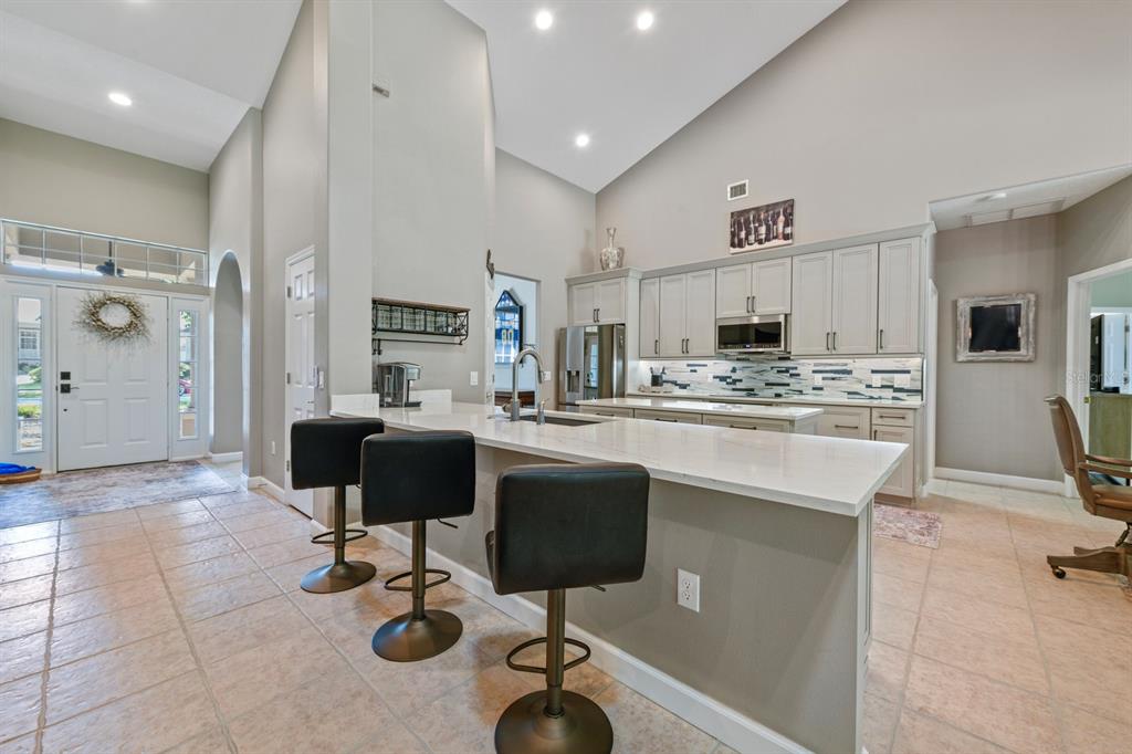 A kitchen with a large island, bar seating, light cabinetry, and high vaulted ceilings — 5039 GREENBRIAR TRAIL, MOUNT DORA, FL