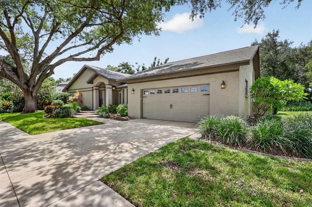 A single-story house with a beige stucco exterior, a two-car garage, and a large tree — 4395 OAK VIEW DRIVE, SARASOTA, FL