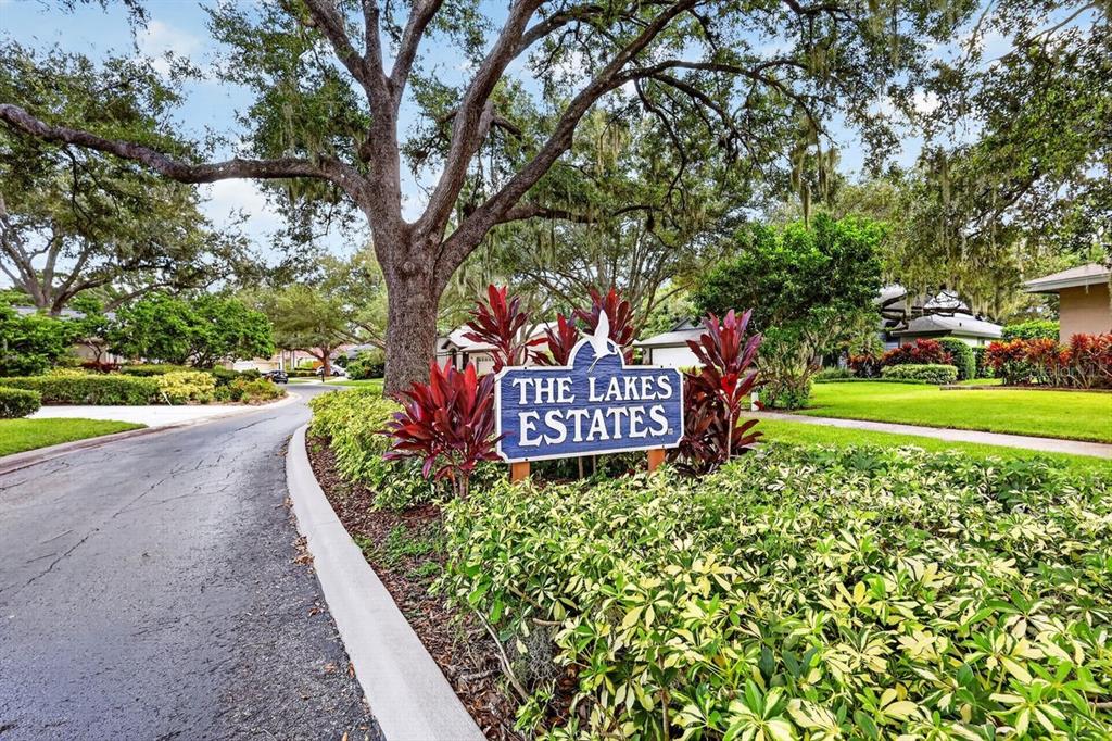 A sign for The Lakes Estates stands in a landscaped garden beside a paved road — 4395 OAK VIEW DRIVE, SARASOTA, FL