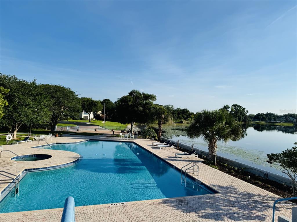 An outdoor swimming pool and hot tub overlook a lake surrounded by trees and landscaping — 1000 WINDERLEY PLACE UNIT 128, MAITLAND, FL