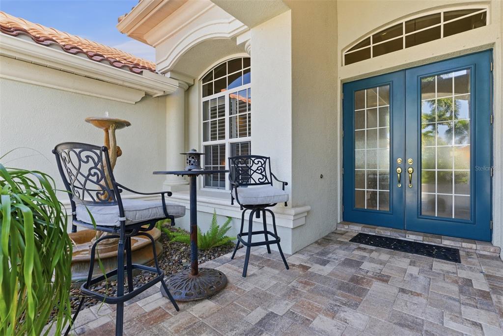 A patio with a small table, two chairs, a fountain, and blue double entry doors — 120 12TH AVENUE E, PALMETTO, FL