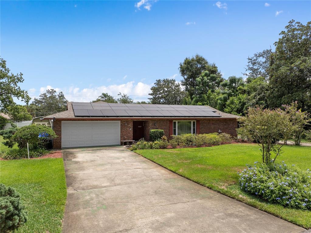 A single-story brick house with a large solar panel array on the roof and driveway — 1435 PAULA DRIVE, APOPKA, FL