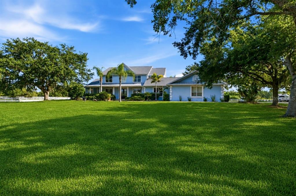 A large, light blue two-story house sits behind a vast, manicured green lawn — 20207 77TH AVENUE E, BRADENTON, FL
