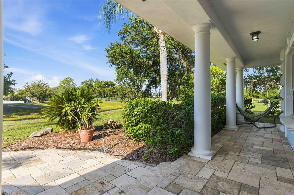 A stone-paved covered porch features white columns, a hammock, and a view of the yard — 20207 77TH AVENUE E, BRADENTON, FL