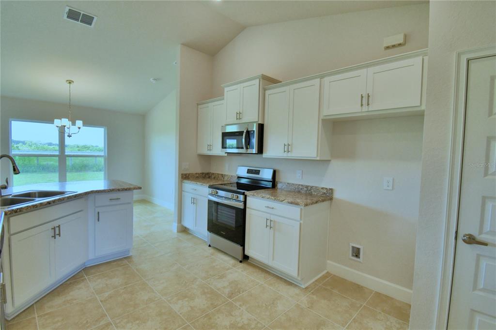 A kitchen features white cabinets, granite countertops, stainless steel appliances, and tile flooring — 4607 CALAMINT LANE, AUBURNDALE, FL