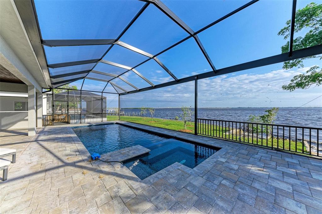 A screened-in patio features a swimming pool with an integrated spa overlooking a large lake — 116 NORTHSHORE TERRACE, PORT CHARLOTTE, FL