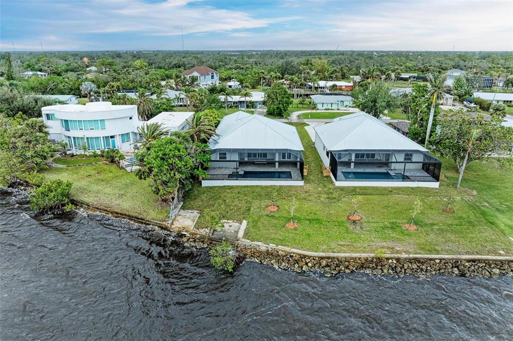 An aerial view shows three waterfront houses with pools and a stone seawall — 116 NORTHSHORE TERRACE, PORT CHARLOTTE, FL