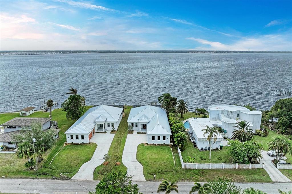 An aerial view shows three waterfront houses with white roofs and lawns along a large body — 116 NORTHSHORE TERRACE, PORT CHARLOTTE, FL