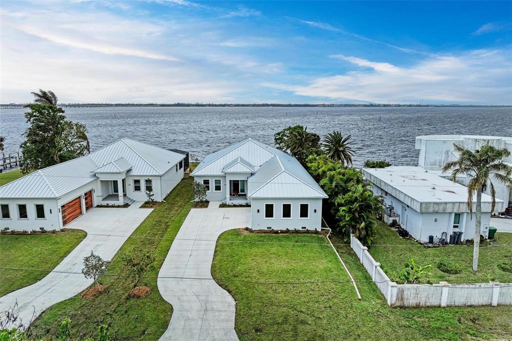 An aerial view shows two modern houses with metal roofs situated along a waterfront — 116 NORTHSHORE TERRACE, PORT CHARLOTTE, FL